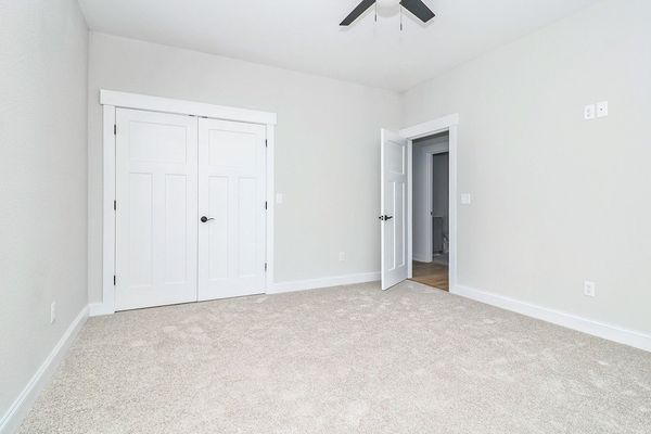 Empty bedroom with white walls, doors, and light carpet. A door leads to another room.