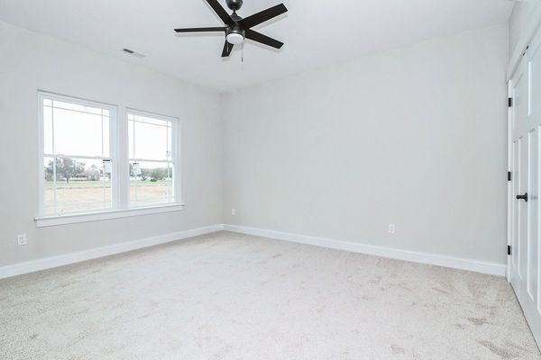 Empty bedroom with light carpet, white walls, two windows, and a ceiling fan.