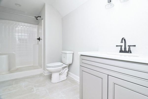 A white and gray bathroom with a shower, toilet, and vanity.