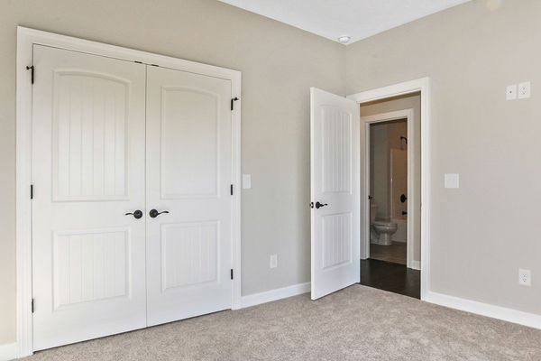Bedroom with white double closet doors, a door to a bathroom, and light carpet on the floor.