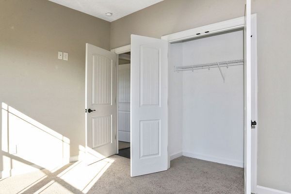 Empty bedroom with open doors: closet and doorway to another room. Neutral colors, carpet.