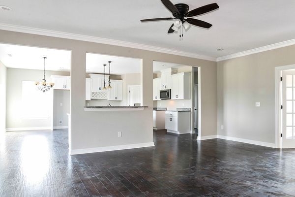 Empty living room with dark wood floor, light gray walls, and open view to kitchen.