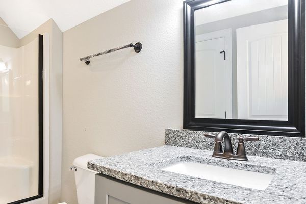 Bathroom with a gray vanity, granite countertop, rectangular mirror with a black frame, and a chrome faucet.