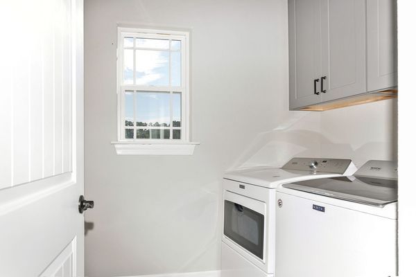 Laundry room with white washer and dryer, grey cabinets, and window with a view.