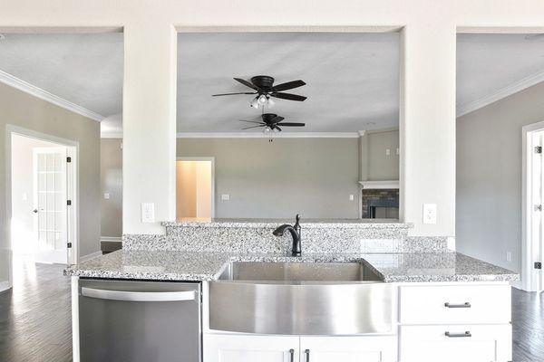 Kitchen with stainless steel sink, granite countertop, and view through a rectangular opening to the living room with ceiling fans.
