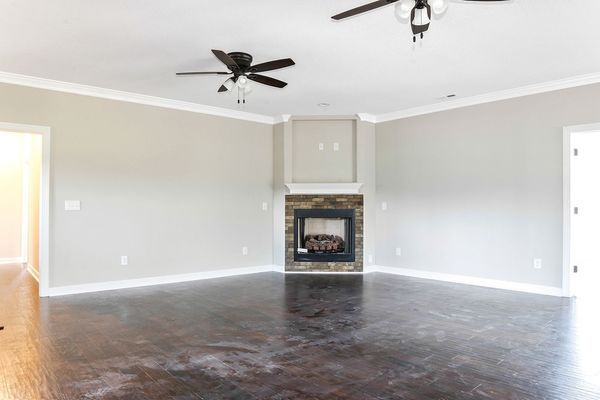 Empty living room with dark flooring, fireplace, two ceiling fans, and light gray walls.