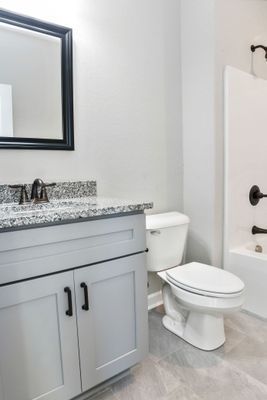 Bathroom with light gray walls, white toilet and tub, and light gray vanity with black accents.