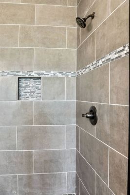Shower with gray rectangular tiles, built-in shelf, bronze shower head and faucet.