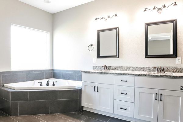 Bathroom with a white vanity, a grey tile-surrounded bathtub, and two framed mirrors.
