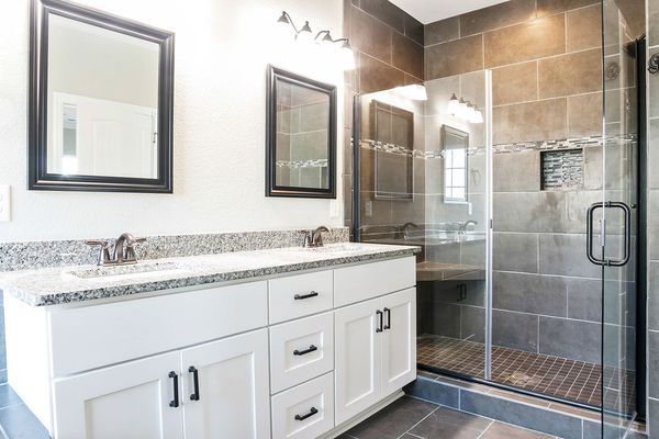 Bathroom with white vanity, dark gray shower with glass door, and two mirrors.