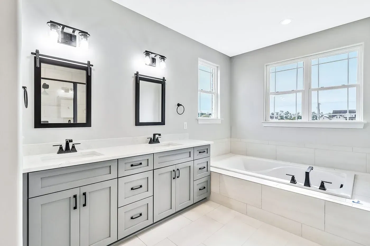 Bathroom with light gray cabinets, white countertops, black fixtures, and two mirrors.