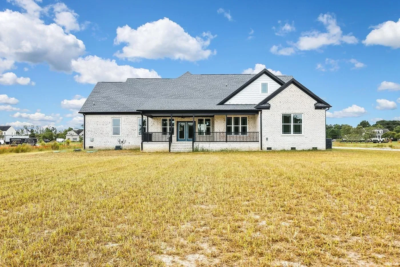 Light brick house with a dark roof and black trim, set in a grassy field under a blue sky with clouds.