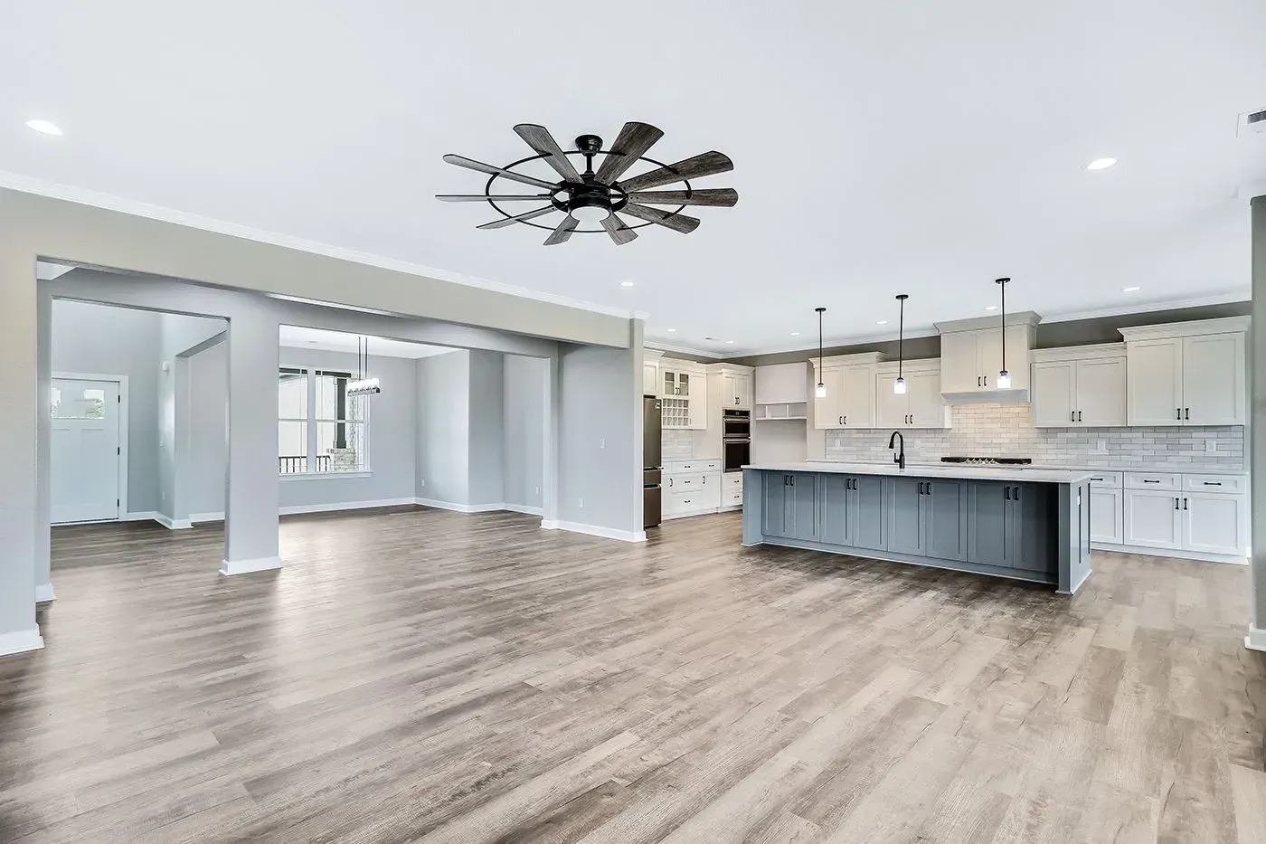 Spacious kitchen and living area with gray cabinets, wood floors, and a modern ceiling fan.