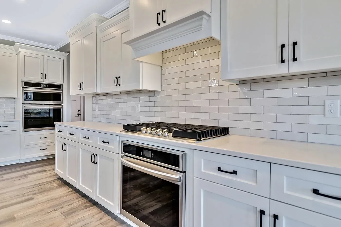White kitchen with white cabinets, stainless steel appliances, and white brick backsplash.