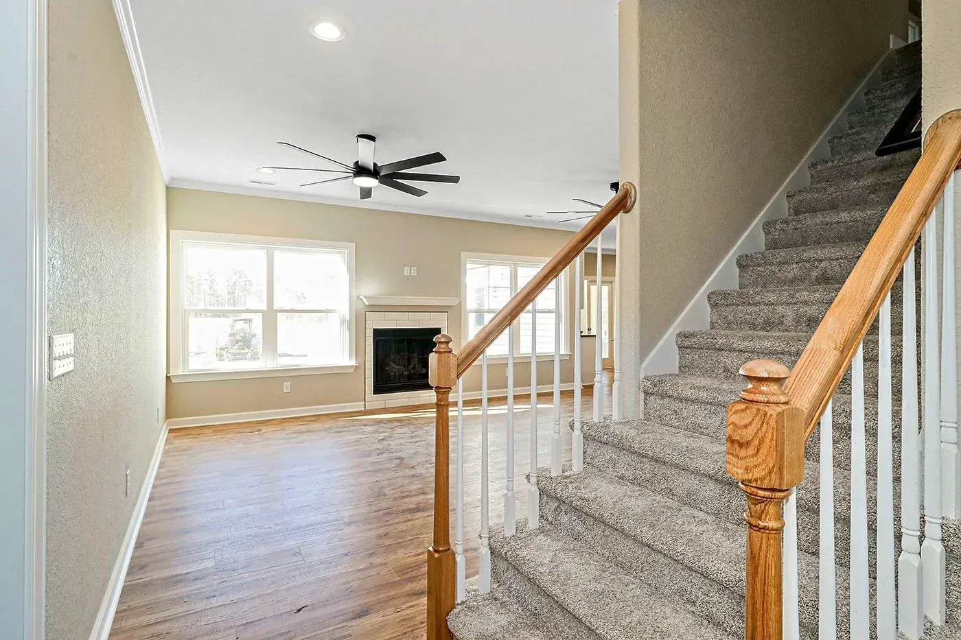 View from a staircase landing into a living room with a fireplace and windows; hardwood floors, neutral walls.