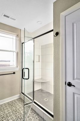 Modern bathroom with glass shower, white walls, patterned floor, and window.