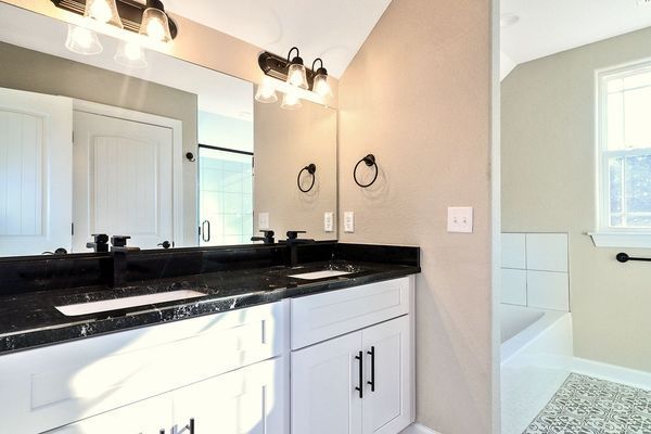 Bathroom with double vanity, black countertop, white cabinets, large mirror, and recessed lighting.