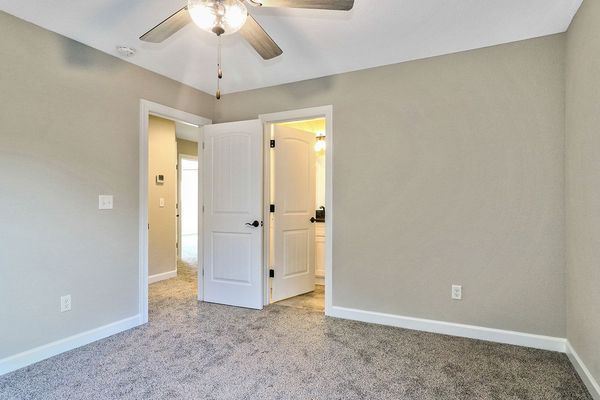 Empty bedroom with carpet, light gray walls, white doors, and a ceiling fan.