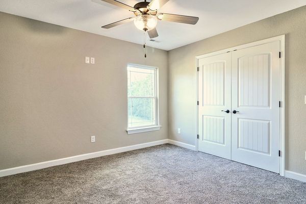 Empty bedroom with gray walls, carpet, window, ceiling fan, and white closet doors.