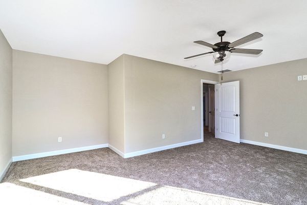 Empty beige bedroom with carpet, ceiling fan, and door.