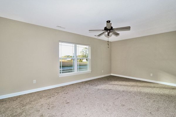 Empty room with beige walls, carpet, and a ceiling fan, with a window and white trim.
