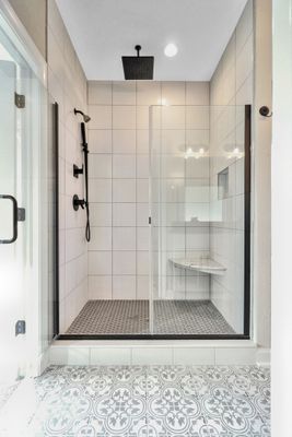Modern shower with black fixtures and white tile, glass door, built-in seat, patterned floor.
