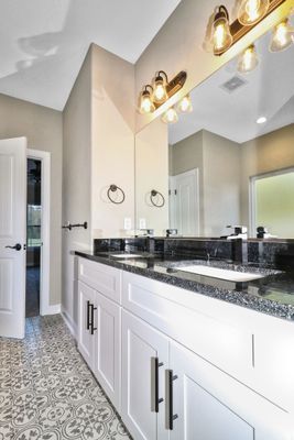 Bathroom with white vanity, black countertop, patterned floor, and large mirror.