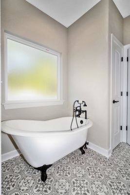 White clawfoot bathtub in a corner bathroom, with patterned floor, window, and door.