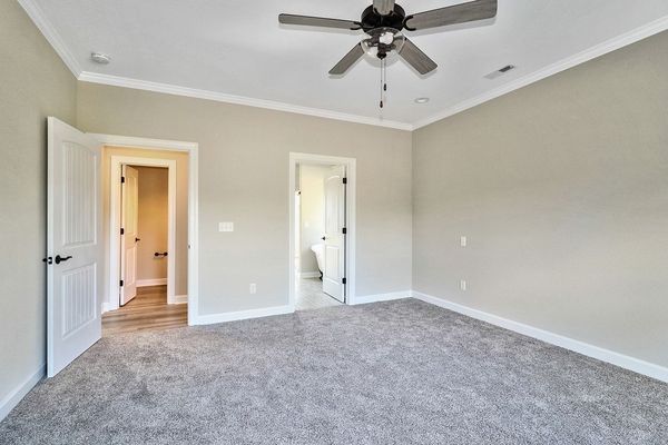 Empty bedroom with light gray walls, gray carpet, and two open doorways. White trim and ceiling fan present.