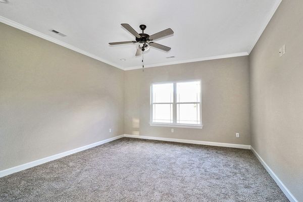Empty bedroom with neutral walls, gray carpet, and a ceiling fan.