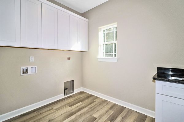 Laundry room with white cabinets, window, washing machine connections, and wood-look flooring.