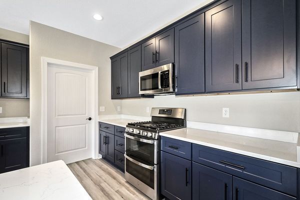 Kitchen with navy blue cabinets, stainless steel appliances, and white countertops and door.