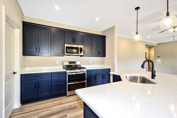 Modern kitchen with dark blue cabinets, white countertops, and stainless steel appliances.