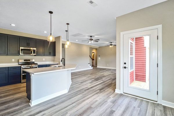 Modern kitchen with dark cabinets, white countertop, and gray wood-look flooring. Door to outside.