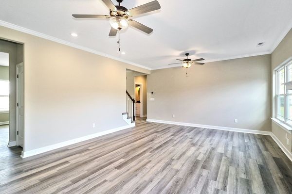 Empty living room with wood-look flooring, beige walls, white trim, and two ceiling fans.