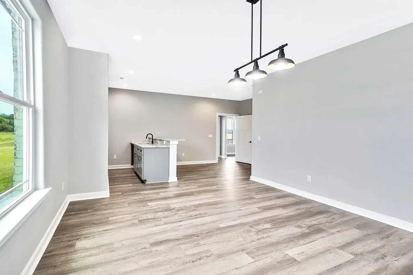 Empty dining area with gray walls, light wood-look floor, island, and hanging lights.