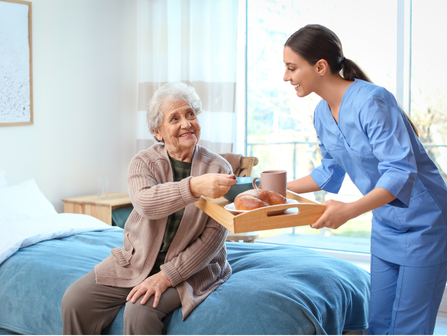 Nurse serving a drink to a patient sitting on a hospital bed in a bright room