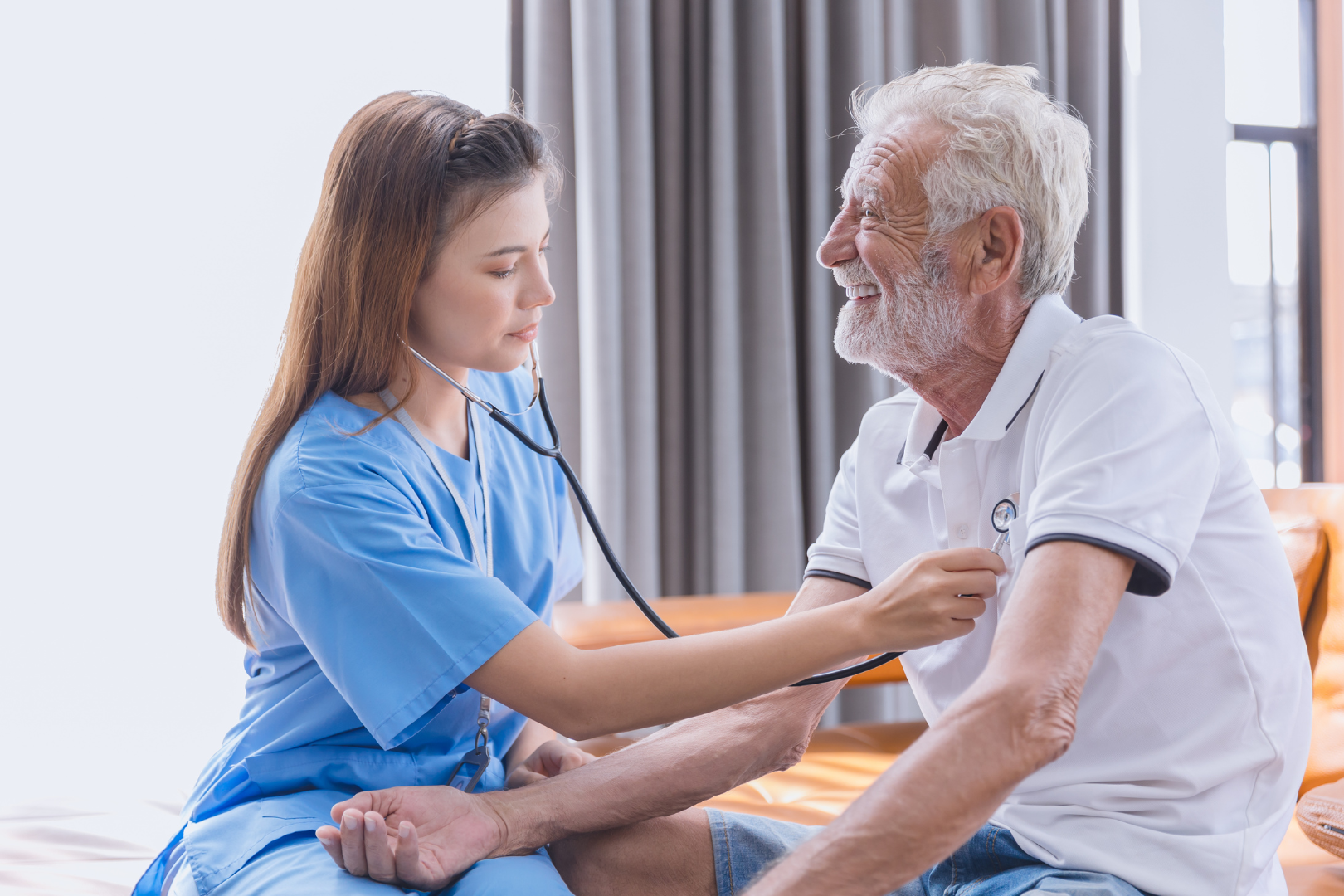 Nurse in blue checks an elderly man's blood pressure in a bright room
