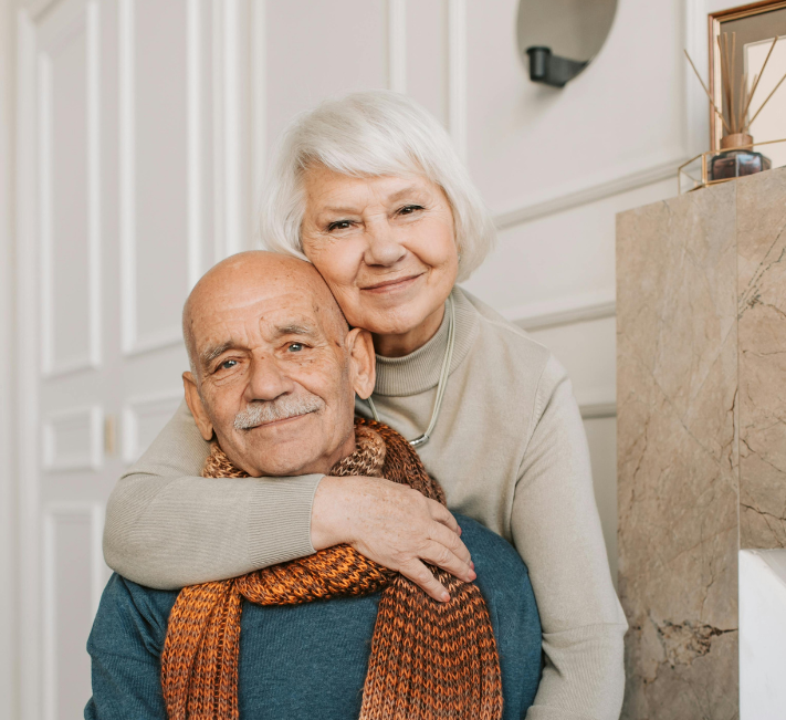 Smiling couple embracing indoors, with the woman hugging the man from behind.