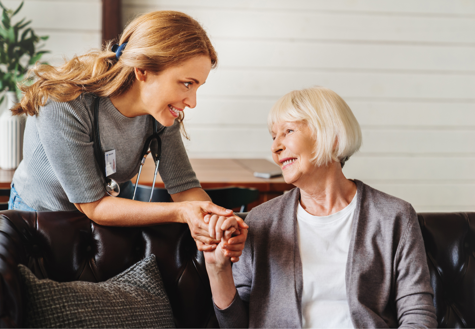Two women smiling and holding hands on a couch in a cozy living room