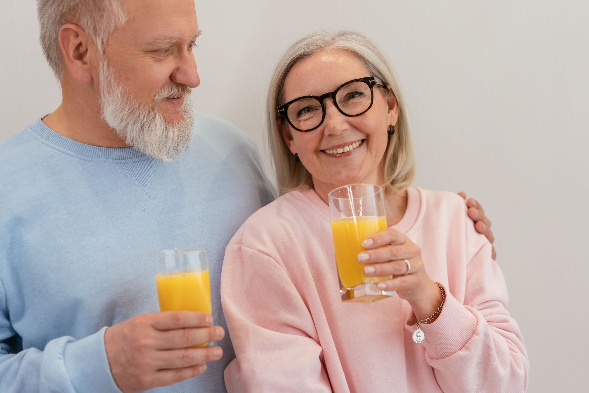 Two smiling people holding glasses of orange juice against a light background