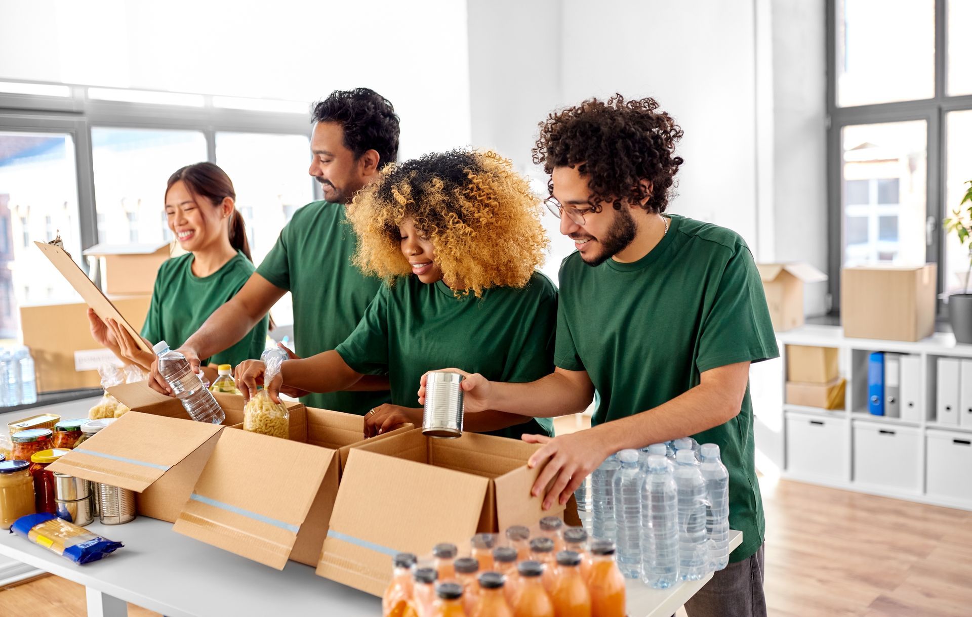 Volunteers in green shirts packing food into boxes in a bright room. Volunteers in green shirts packing food into boxes in a bright room.