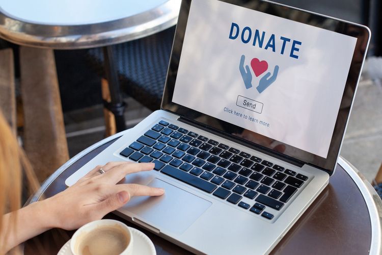 Person using a laptop to donate online; a white cup of coffee sits to the left.