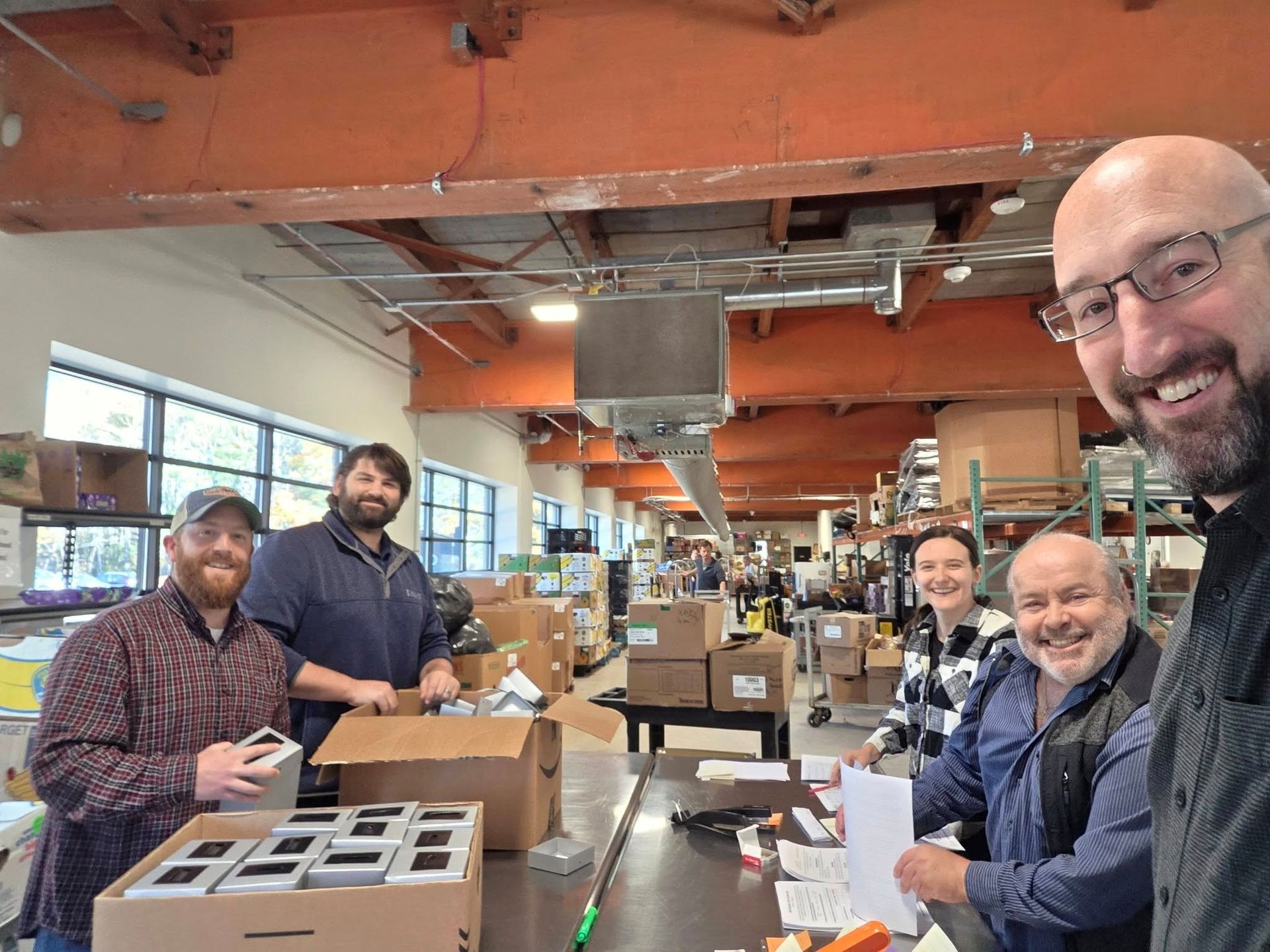 Five people packing boxes in a warehouse with an overhead crane. They are smiling and working. Five people packing boxes in a warehouse with an overhead crane. They are smiling and working.
