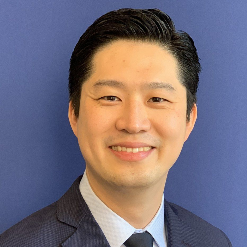 Smiling man in a navy suit and light blue shirt against a blue background