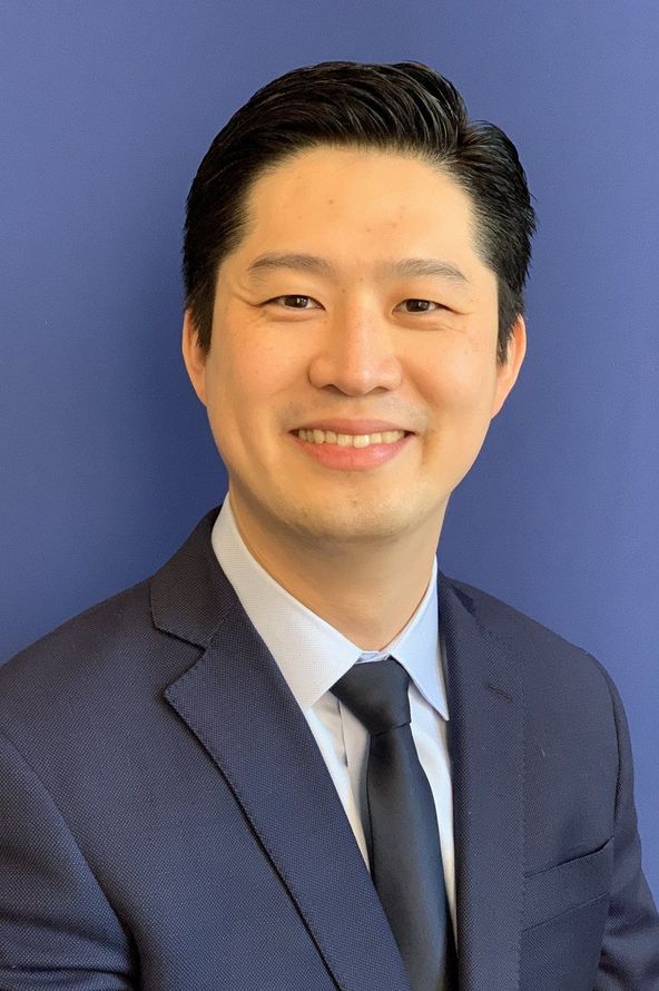 Smiling man in a navy suit and tie against a blue background