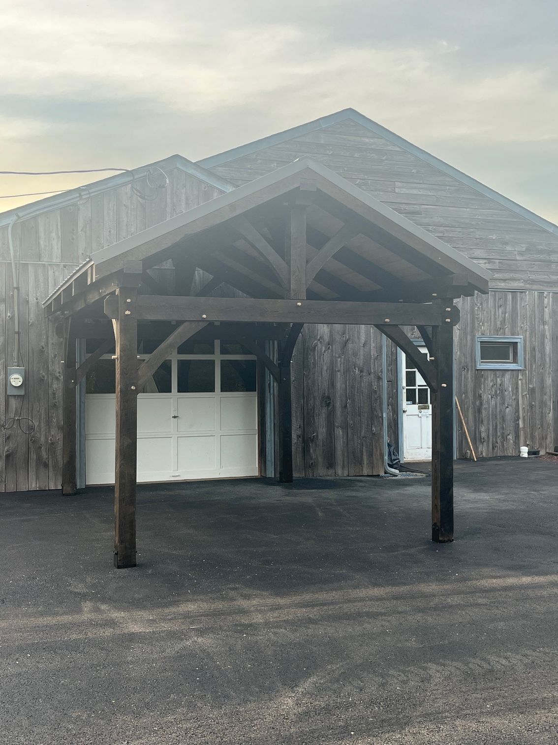 A wooden timber-frame portico extends over a white garage door against a grey, weathered-wood barn building. Pennsylvania 