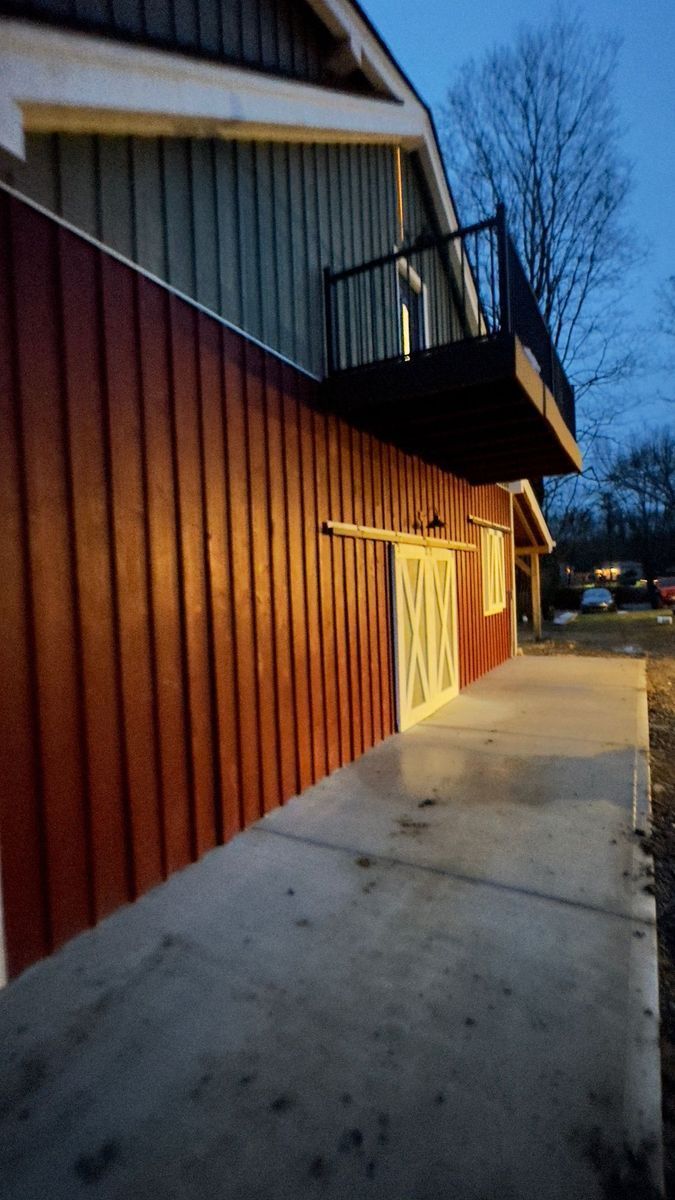 A rustic barn with red vertical siding,a concrete walkway, made by Central Timber Frame Supply. 