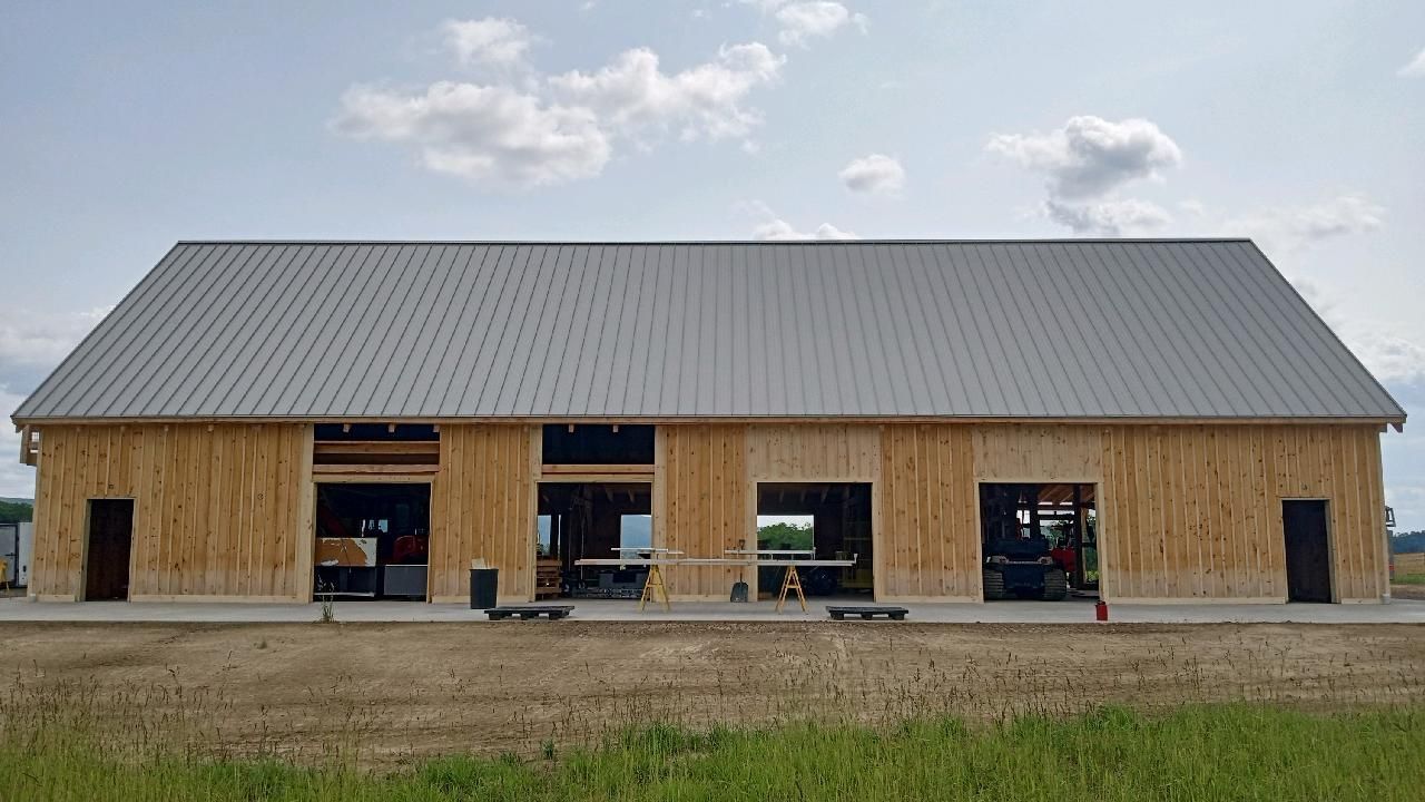 A large, newly constructed Amish wooden barn with a gray metal roof by Central Timber Frame Supply. 