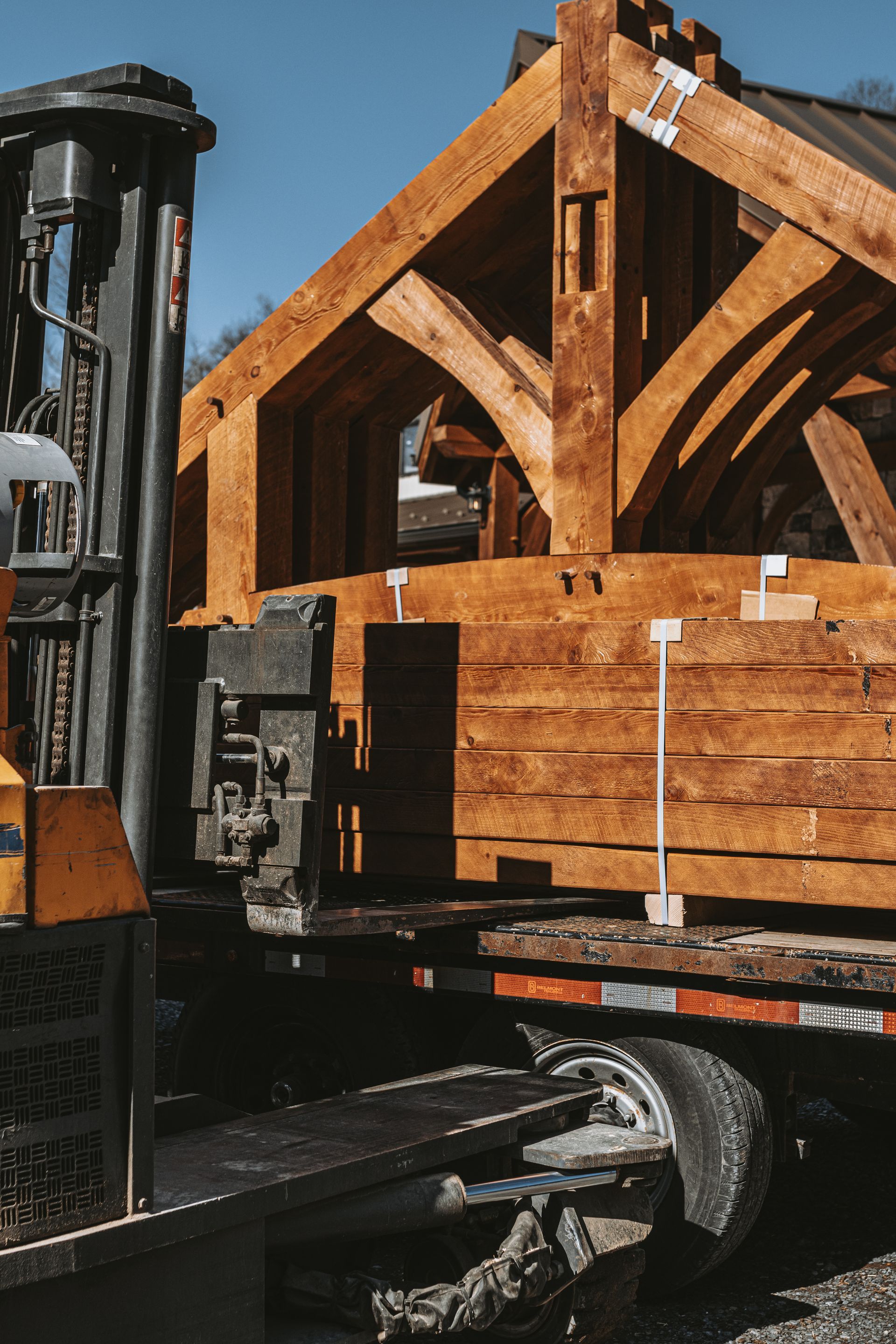 Unfinished wooden timber-frame structure on a trailer outdoors under a clear blue sky. By Central Timber Frame Supply. 